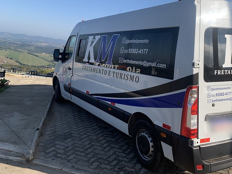 Van da KM Fretamento e Turismo vista de trás e de lado, estacionada em um mirante com vista para as montanhas